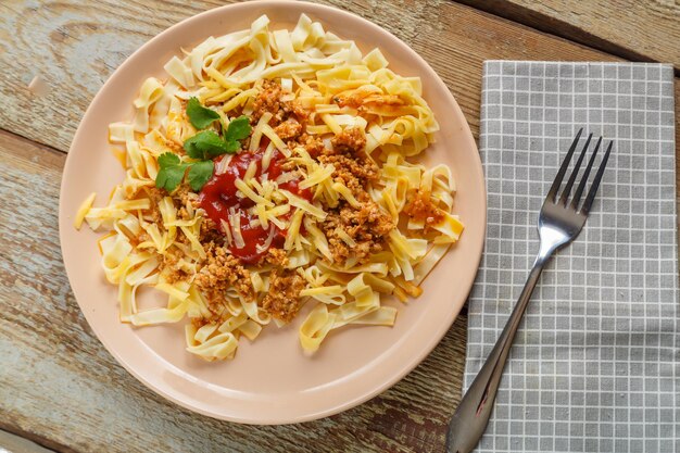 Macarrão à bolonhesa em tomate guarnecido com ervas e queijo em um prato sobre uma mesa de madeira