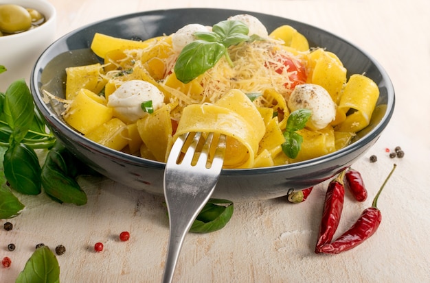 macarrão amarelo cozido pappardelle, fettuccine ou tagliatelle no garfo. Ovo de macarrão caseiro com fita ou macarrão com tomate, bolas de manjericão e mussarela