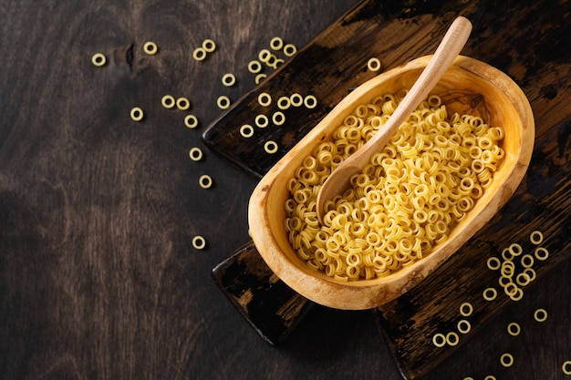 Macarrão Anellini em uma tigela de madeira de oliva na velha mesa de madeira. Conceito de cozinha. Vista superior com espaço de cópia.