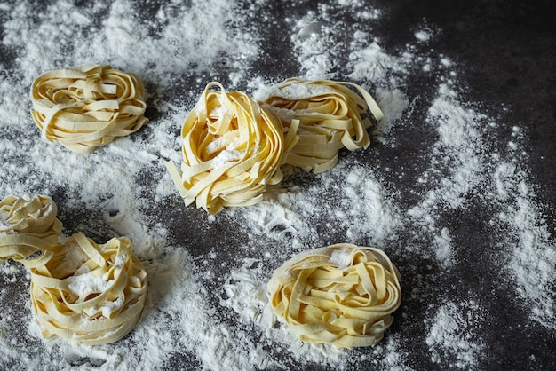 Macarrão artesanal de tagliatelle cru com farinha em mesa escura