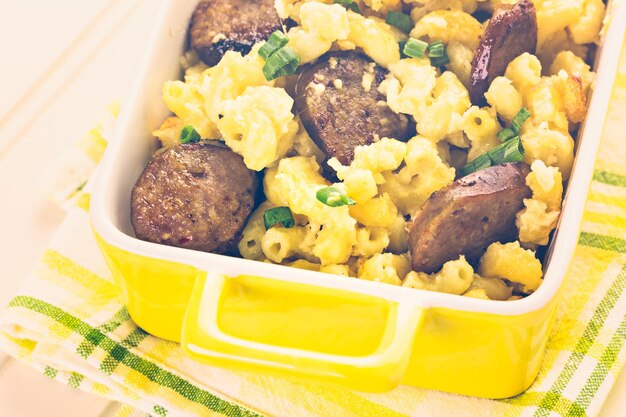 Macarrão assado com queijo com linguiça italiana e guarnecido com cebolinhas.