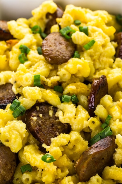 Macarrão assado com queijo com linguiça italiana e guarnecido com cebolinhas.