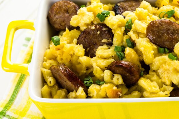 Macarrão assado com queijo com linguiça italiana e guarnecido com cebolinhas.