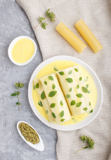 Macarrão canelone com molho de ovo, queijo creme e folhas de orégano em concreto cinza