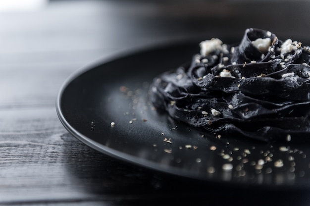 Macarrão caseiro preto de delicadeza com queijo feta e ervas provençais em um prato preto