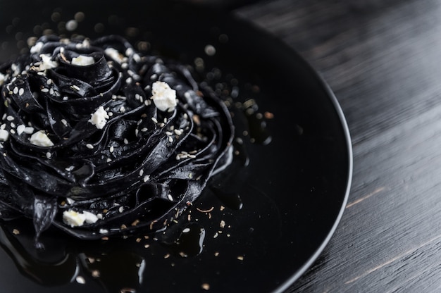 Macarrão caseiro preto de delicadeza com queijo feta e ervas provençais em um prato preto