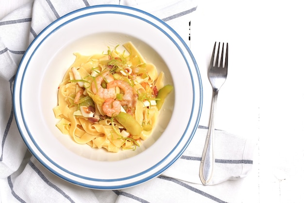 Macarrão com abobrinha e frutos do mar em um prato branco com um garfo em um pano de cozinha no fundo branco