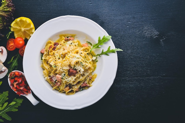 Macarrão com bacon tomate cereja azeitonas e cogumelos com queijo parmesão comida italiana em uma superfície de madeira preta espaço livre para o seu texto vista superior