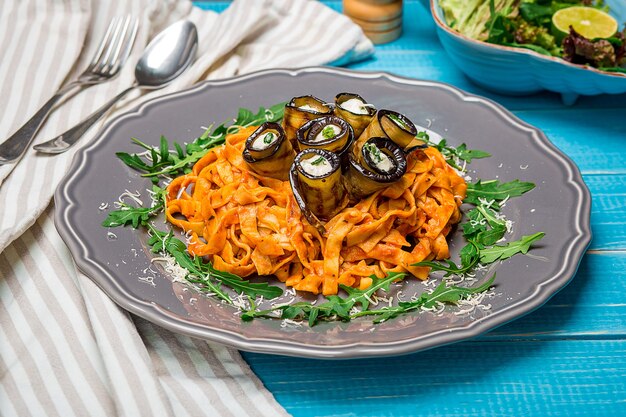 Macarrão com berinjela, tomate, queijo e rúcula. A apresentação original do prato do chef. Sobre um fundo azul de madeira.