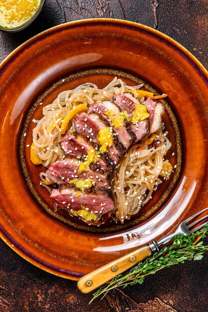 Macarrão com bife de filé de peito de pato num prato. mesa escura. vista do topo.