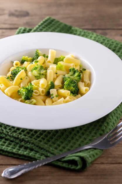 Macarrão com brócolis em um prato branco e mesa de madeira