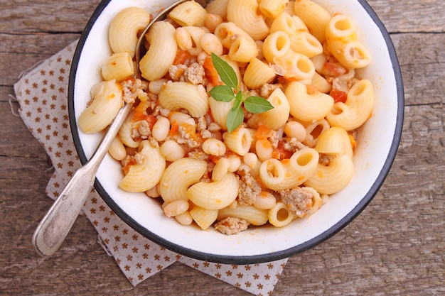 Macarrão com carne e feijão em uma tigela branca sobre o fundo de madeira velha