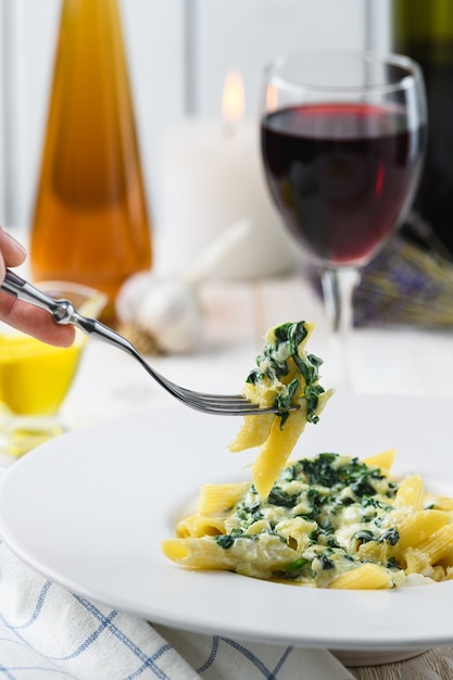 Macarrão com espinafre mussarela e vinho sobre um fundo claro.