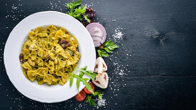 Macarrão com espinafres, azeitonas e cogumelos com queijo parmesão. Comida italiana. Em uma superfície de madeira preta. Espaço livre para o seu texto. Vista do topo.