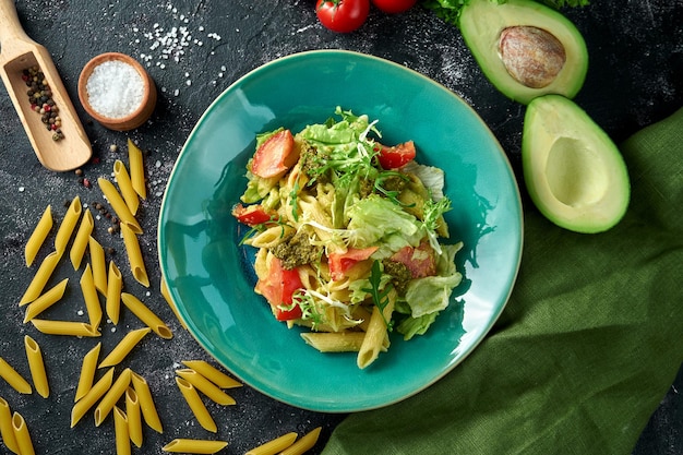 Macarrão com legumes, tomate e pesto em um prato sobre fundo escuro Salada com macarrão