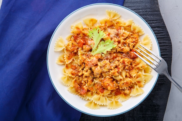 Macarrão com molho de tomate à bolonhesa em um suporte redondo preto em um guardanapo azul ao lado de um garfo Foto horizontal