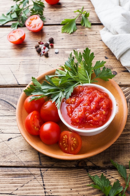Macarrão com molho de tomate em uma tigela e tomates frescos com salsa em uma mesa de madeira