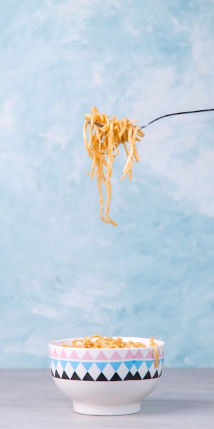 Macarrão com molho em uma tigela colorida, a mão segura um garfo de macarrão pendurado, espaguete de apetite em azul.