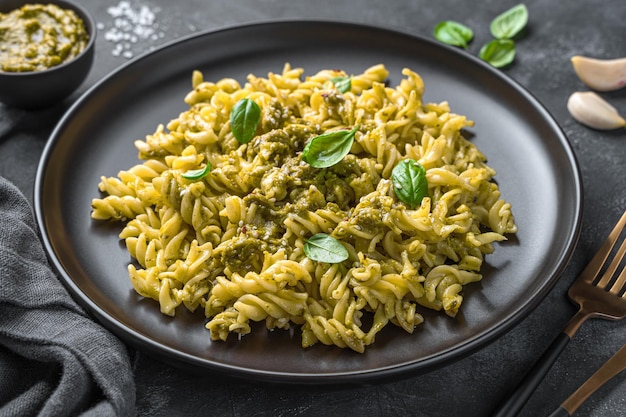 Macarrão com molho pesto folhas de manjericão fresco e sementes de gergelim em um fundo escuro