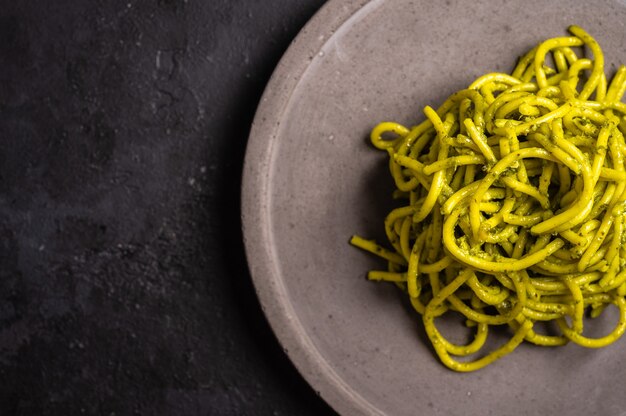 Macarrão com pesto close-up servido em prato de cerâmica cinza com foco seletivo de fundo texturizado escuro