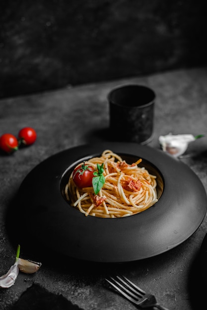 Macarrão com queijo feta e tomate assado em prato preto espaguete