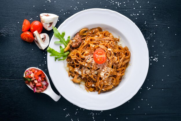 Macarrão com tomate cereja azeitonas e cogumelos com queijo parmesão Comida italiana Em uma superfície de madeira preta Espaço livre para o seu texto Vista superior