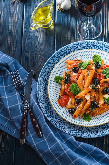 Macarrão com tomate cereja, azeitonas mussarela e espinafre, vinho e azeite em uma mesa de madeira. Estilo rústico.