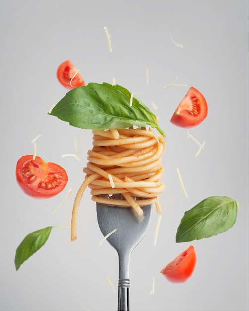 macarrão com tomate e manjericão em um garfo com levitando tomate e manjericão