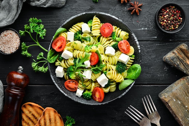 Macarrão com tomate espinafre e queijo feta Em um prato preto sobre um fundo de madeira Vista superior Espaço livre para o seu texto Postura plana