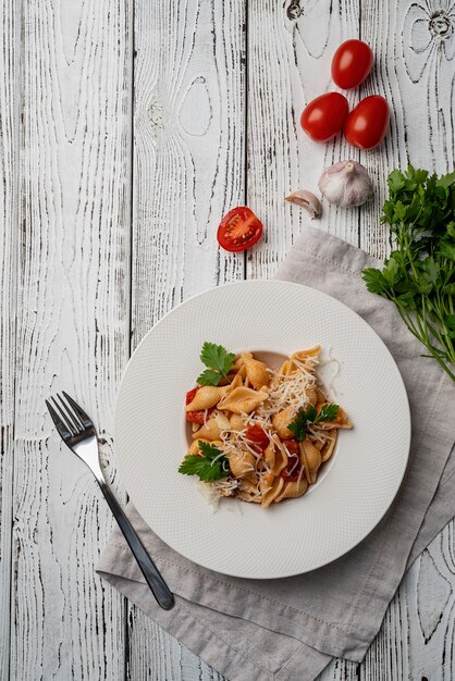 Macarrão Conchiglioni com tomate cereja, queijo e salsa em prato branco sobre fundo de madeira