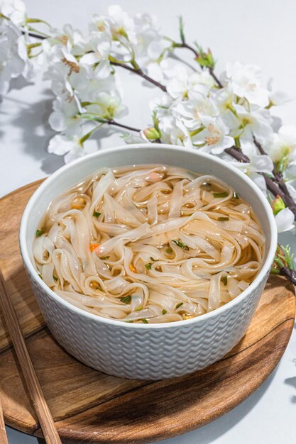 Macarrão coreano Ramen com caldo Prato quente pauzinhos luz dura sombra escura Fundo cinza flores de cerejeira planas close-up