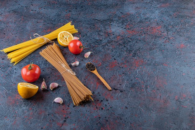Macarrão cru com tomate vermelho fresco e alho em um fundo escuro.