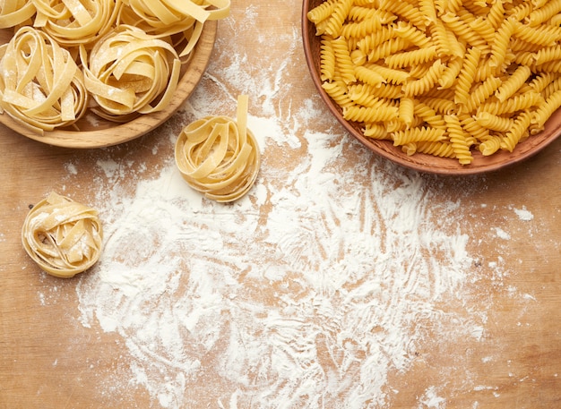 Macarrão cru fusilli e fettuccine em placas de madeira sobre uma mesa de madeira marrom