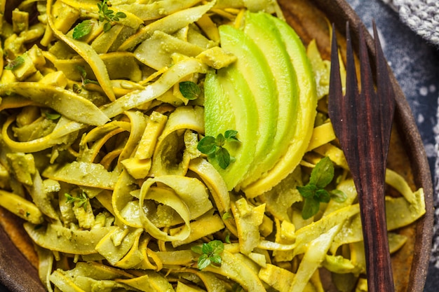 Macarrão de abobrinha com pesto e abacate no prato escuro. comida vegetariana saudável.