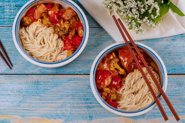 Macarrão de arroz com frango frito e legumes em tigelas e pauzinhos