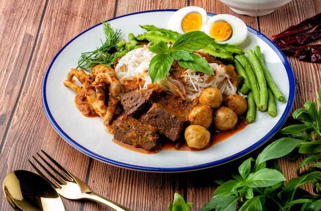 Macarrão de arroz com molho de caril de peixe, cubra com almôndega, cubos de sangue de frango, pés de frango, ovo cozido e muitos vegetais. Comida tailandesa, os tailandeses chamam de "Kanom Jeen Nam Ya". Decore o prato bonito para servir.