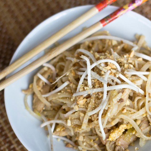 Macarrão de arroz coreano com brotos de soja e amendoim moído em uma tigela branca com pauzinhos