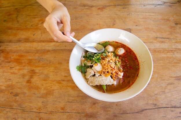 Macarrão de arroz em sopa picante com bola de carne de porco, legumes e carne de porco servindo na mesa de madeira na cantina