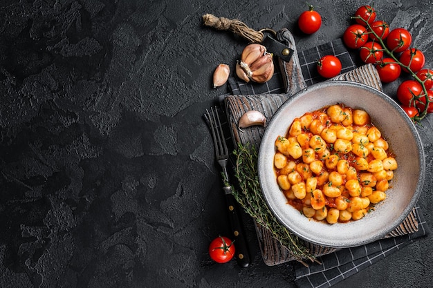 Macarrão de batata nhoque com molho de tomate e tomilho. Fundo preto. Vista do topo. Copie o espaço.