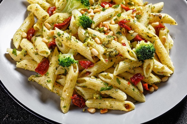 Macarrão de brócolis pesto penne com tomate seco e pinhões em um prato, vista horizontal de cima, cozinha italiana, close-up