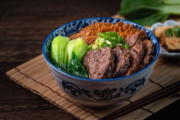 Macarrão de carne de comida famosa taiwanesa com pernil de carne assada fatiado, tripa e legumes no fundo da mesa de madeira.