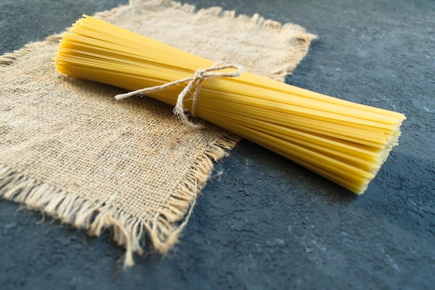 Macarrão de espaguete cru amarrado com uma corda em um fundo de textura preta.