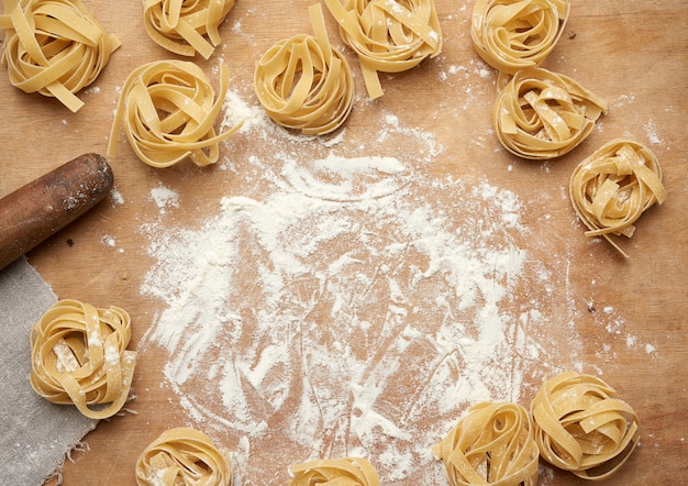 Macarrão de fettuccine cru em uma placa de madeira marrom com farinha branca