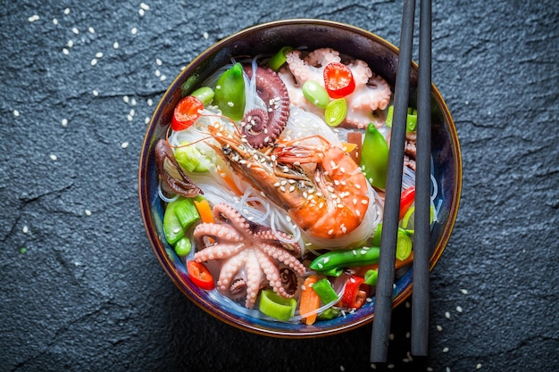 Macarrão de frutos do mar quente em tigela escura com pauzinhos