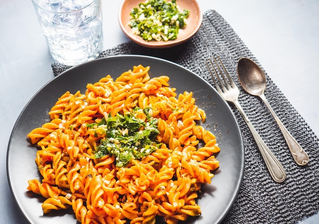 Macarrão de macarrão encaracolado com molho de tomate e gremolata em um prato redondo escuro sobre uma mesa