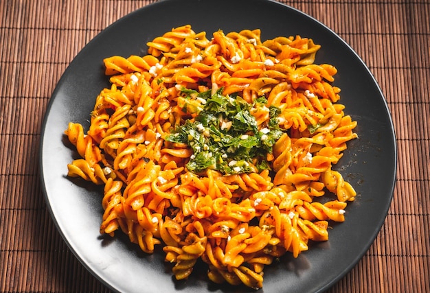 Macarrão de macarrão encaracolado com molho de tomate e gremolata em um prato redondo escuro sobre uma mesa