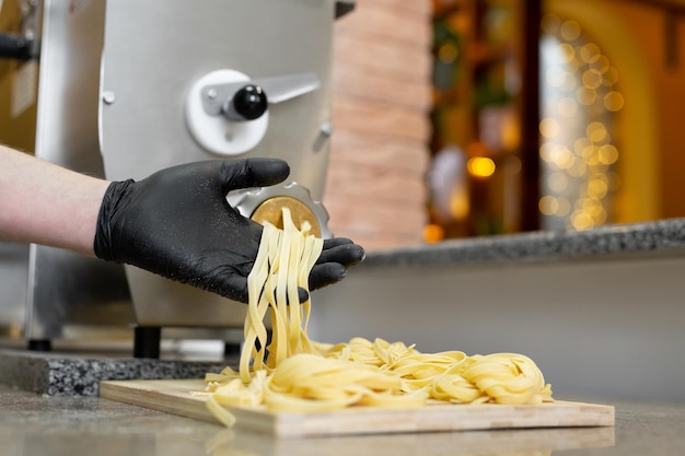 Macarrão de macarrão sai de uma máquina profissional, abre e torce em uma placa de madeira