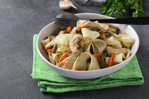 Foto macarrão de ovo com legumes de frango e especiarias em um prato leve em fundo cinza