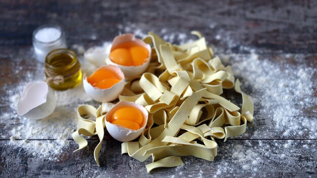 Macarrão de ovo, farinha, ovos em cima da mesa.