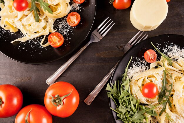 Macarrão de tagliatelle italiano ao lado de tomate cereja em fundo de madeira